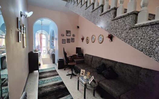 Ingresso di una casa a schiera a Malta con scala in granito e zona soggiorno accogliente con divano morbido e cornici decorative.
