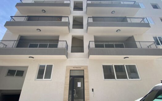 Facciata di un moderno edificio residenziale a Malta, mostrando il design esterno degli attici con ampi balconi e l'ingresso principale etichettato "Da Vincenzo"