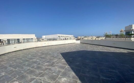 Ampia terrazza panoramica di un attico situato a Qawra, con pavimentazione in piastrelle di ardesia grigia e balaustra in cemento, che offre una vista aperta e un ampio potenziale per l'intrattenimento all'aperto.