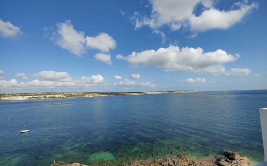 Vista dal terrazzo di un attico a Malta che si affaccia sul mare sereno, con il cielo azzurro punteggiato da nuvole bianche soffici.
