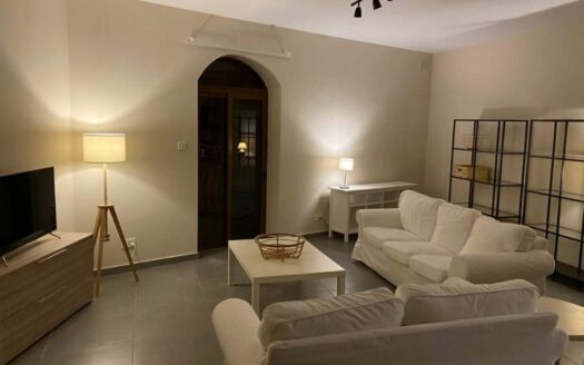 Un accogliente soggiorno di un quadrilocale a Malta, con divani bianchi, una lampada da terra stilizzata e un separè decorativo. La stanza è illuminata da una luce calda che crea un'atmosfera intima, con una porta in legno che suggerisce l'accesso ad altre aree dell'appartamento.