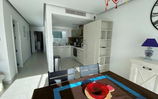 Cucina moderna e luminosa di un appartamento a Malta, con mobili bianchi, pavimento in piastrelle e decorazioni colorate.